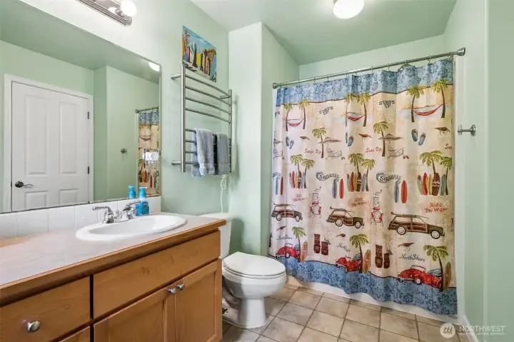 The exterior door leading directly out to the yard and outdoor shower setup makes cleanup after swimming, paddleboarding or sandy beach days ridiculously convenient. Rinse off outside first, then step right into the bathroom without trekking water through the whole house like a determined little lake raccoon. Inside, the long vanity gives you plenty of counter space to spread out comfortably. The room keeps the same warm, cohesive finishes carried throughout the home too, so even the practical spaces still feel polished and thoughtfully designed.