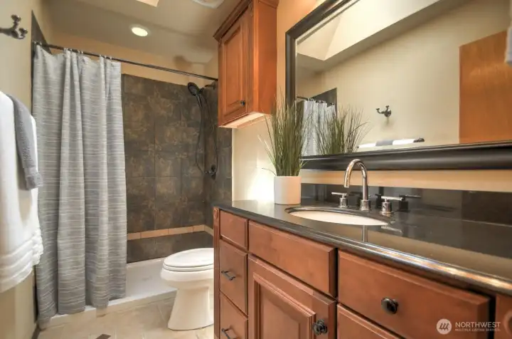 Large hallway bathroom with tiled walk in shower, cherry cabinets and granite countertop.
