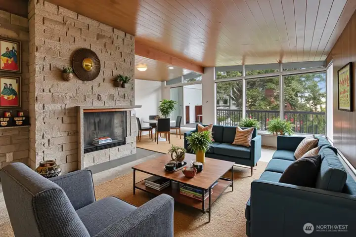 Virtually staged living and dining room. Classic mid-century lines are undeniably appealing. The warm wood ceiling reflects natural light into the living space, and oversized windows are a pleasure. Wood-burning fireplace.
