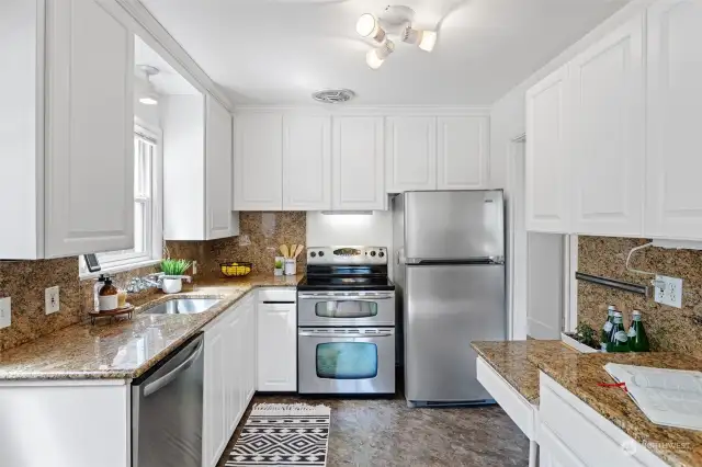 Kitchen has been remodeled with white cabinets, granite slab counters with granite backsplash extending up to cabinets and a large undermount stainless sink.