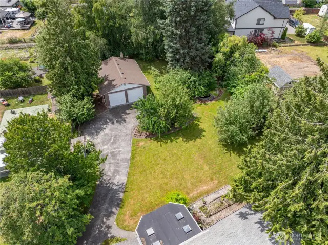 Aerial view of the property showcasing the detached garage, paved driveway, well-maintained lawn and mature shrubs/trees create private setting.