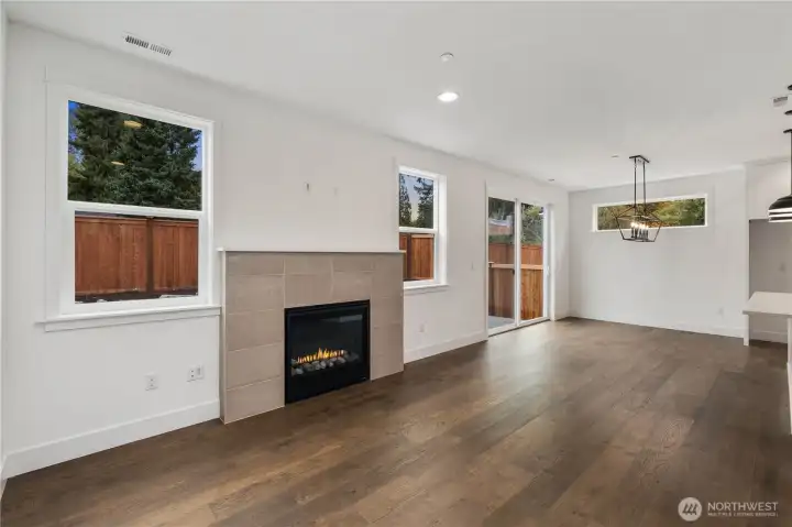 Great Room:  Large windows spill natural light across the great room, highlighting the wide-plank flooring and the gas fireplace wrapped in soft neutral tile. The open flow invites flexible furniture placement and comfortable day-to-day living. With Gooden Hollow’s Bothell location near Canyon Park amenities, this room becomes a peaceful backdrop to Northwest living, surrounded by mature evergreens and convenient access to nearby recreation. Its simplicity and warmth make it equally suited for quiet evenings or effortless entertaining.    These photos are from Lot 5 at Gooden Hollow, the home listed here. However, other homes in the community will have changes, so all photos, renderings, site maps, and floorplans are for visualization purposes only. Plans, colors, building orientation, finishes, home outlook, and other details can and WILL vary.