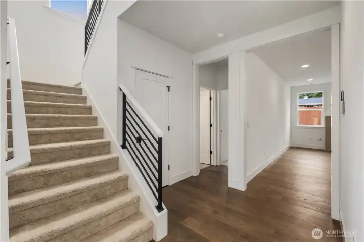 Stairway & Lower Hall:  The wide lower hallway connects key main-level spaces, while the open stairway brings natural light from the upper landing into the heart of the home. Its layout allows for smooth circulation between the great room, kitchen, den, and main-level bedroom. Located in the Canyon Park area of Bothell, the home’s thoughtful design pairs modern architecture with proximity to Northshore schools, commuting corridors, and neighborhood amenities. Clean lines, metal railing accents, and warm flooring lend the hallway a contemporary, welcoming feel.    These photos are from Lot 5 at Gooden Hollow, the home listed here. However, other homes in the community will have changes, so all photos, renderings, site maps, and floorplans are for visualization purposes only. Plans, colors, building orientation, finishes, home outlook, and other details can and WILL vary.