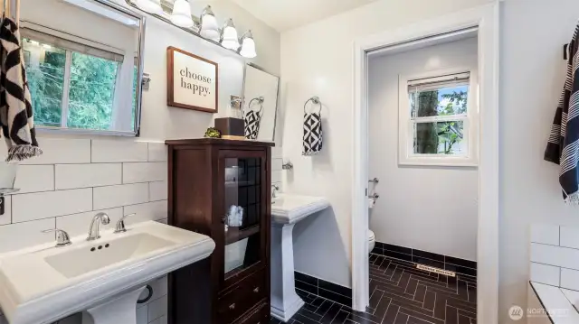 Striking remodeled primary bath with dual pedestal sinks, skylight, and black and white tile work