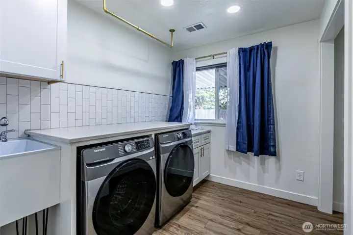 Over the top laundry with sink quartz topped folding counter.  Other details: hang bar above w/d, full storage closet to the right, tile accent strip, storage cabinets.