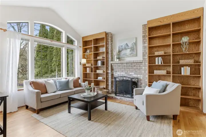 Beautiful living room with large, west facing arched windows and built in bookshelves. Arborvitae provide privacy and soothing green views.