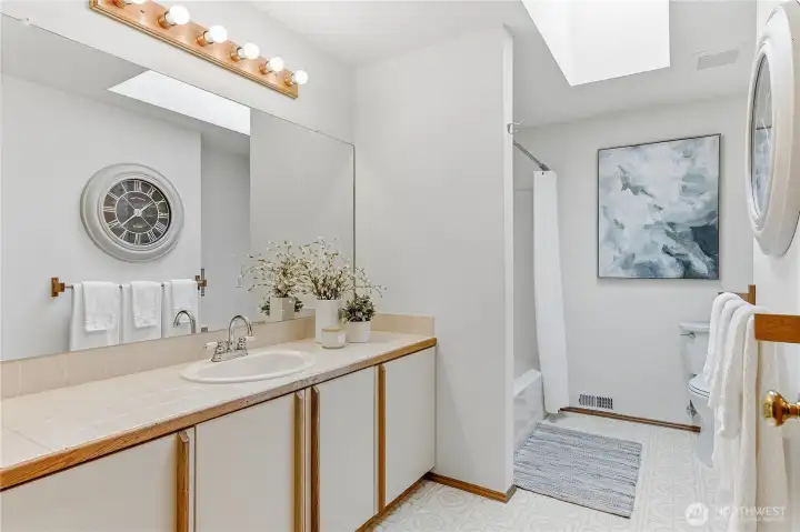 Upstairs guest bathroom features an extra-long vanity with ample storage, a bathtub/shower combo, and a skylight that fills the space with natural light.