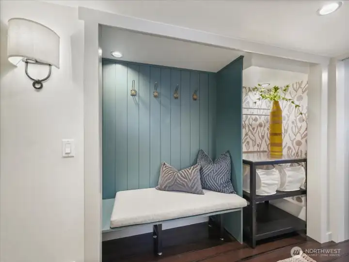 Thoughtfully designed laundry/mudroom features beautiful wood paneling detail, coat hooks, a built-in bench with cushion and stylish wallpaper and a dedicated folding space.