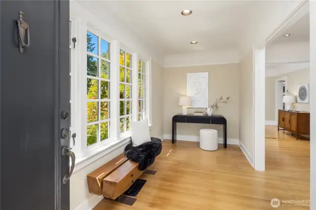 Step into a light-filled foyer facing south toward the lush front yard and blooming roses — a warm and inviting welcome.