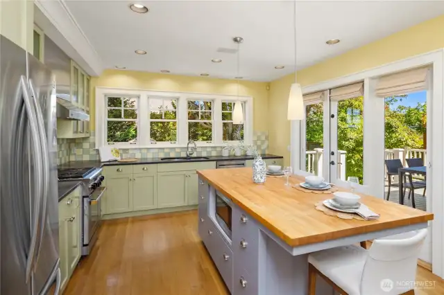 The kitchen features a central island with seating, a wall of windows over the sink, and beautiful windows and glass door opening to the back deck for easy outdoor dining.