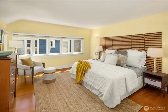 Sunny primary bedroom with warm fir floors and plenty of space for a seating area.