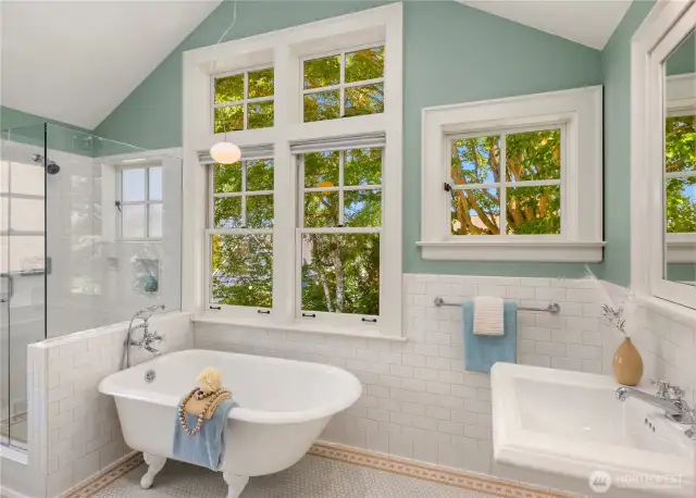 The spa-like primary bath features a clawfoot soaking tub framed by tree-filled views, separate shower, and timeless tile finishes.