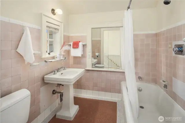 Full upstairs bath with vintage charm, featuring the home’s original pink tile and a classic pedestal sink.