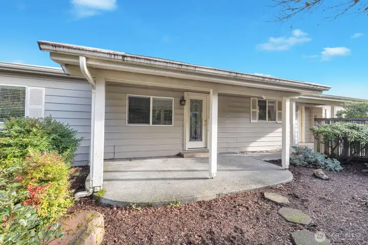 View of the formal entry to the home. The custom etched glass door is off the family room to the covered, private patio area. Room for barbeque, outdoor furniture and more. This yard captures the beauty of nature and all its color!