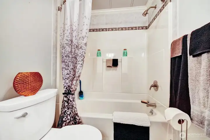 Squeaky clean tub surround with custom tile work at the top in the full guest bathroom that is steps from the guest bedroom and has access door to the utility room.
