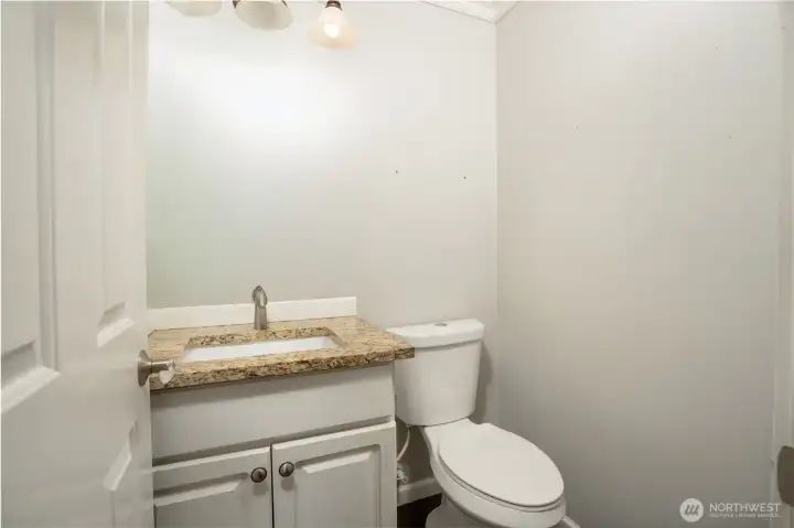Convenient main-level guest bathroom featuring a granite countertop vanity, modern fixtures, and clean neutral finishes. This thoughtfully located powder room offers both style and functionality, providing an ideal space for guests while complementing the home’s overall design and modern feel.