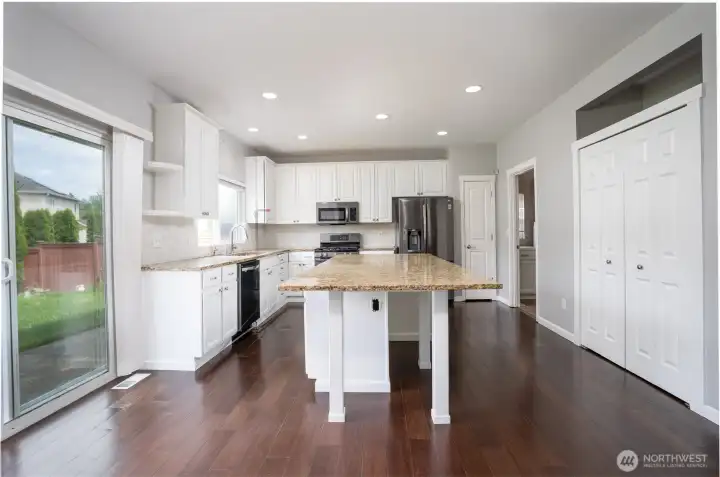 Beautifully designed kitchen featuring an oversized granite island, abundant white cabinetry, the open-concept layout offers ample counter space for cooking, entertaining, and everyday living, while recessed lighting and large windows create a bright and welcoming atmosphere. Sliding glass door access to the backyard makes indoor-outdoor entertaining and summer barbecues effortless.