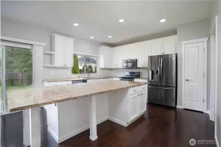 Beautifully designed kitchen featuring an oversized granite island, abundant white cabinetry, ample counter space, and an open-concept layout ideal for cooking, entertaining, and everyday living. Recessed lighting and large windows create a bright and welcoming atmosphere, while the sliding glass door provides easy access to the backyard for seamless indoor-out