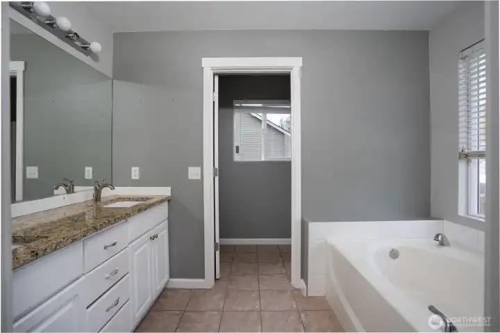 Spacious primary bathroom featuring granite countertops, dual vanity space, a deep soaking tub, separate shower, and plenty of natural light.