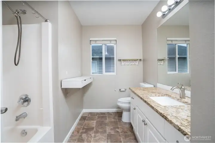 Well-appointed guest bathroom with granite countertops, full tub and shower combo, and a clean functional layout with added storage space.