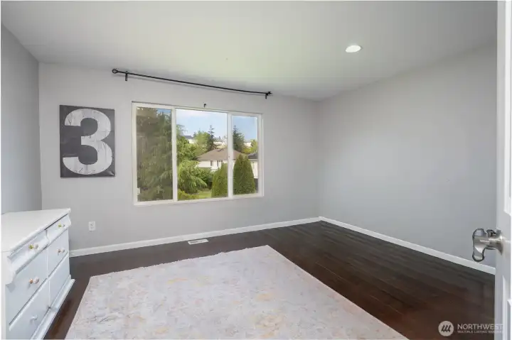 Bright and spacious bedroom with large windows, rich flooring, and plenty of room for a full bedroom setup, office, or flex space.