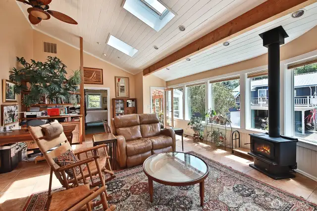 Spacious family room features a wood burning stove and a wall of windows leading to the sun/plant room.