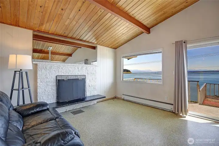 Open living area with exposed beam ceilings, fireplace, and seamless access to the deck with water views beyond.
