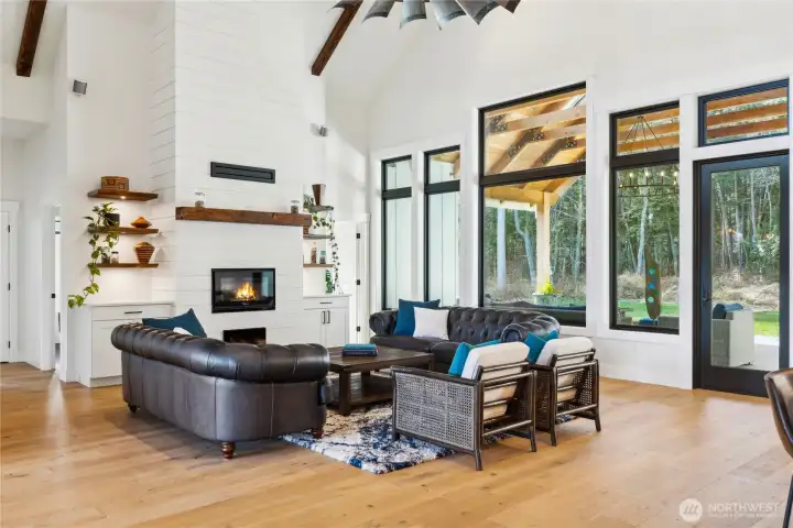 Open and airy living room with cozy wood burning fireplace, vaulted ceilings with wood beams and custom ceiling fan, built-ins and shelving.