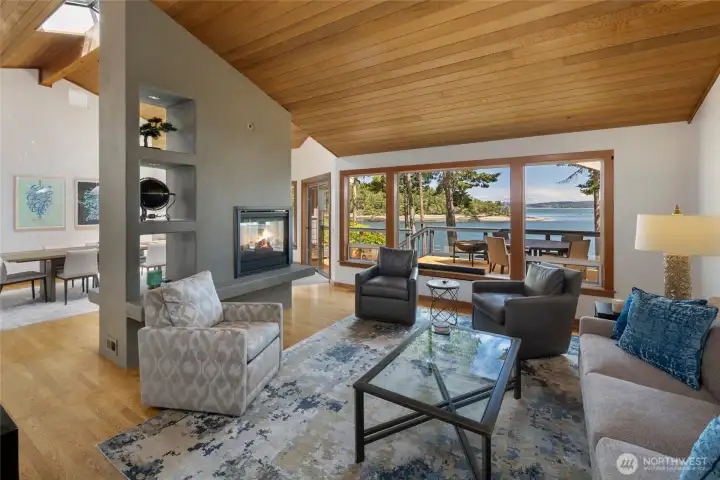 Comfortable living room with vaulted wood ceilings, fireplace, and large windows that bring in natural light while showcasing the property’s serene San Juan Island waterfront setting.