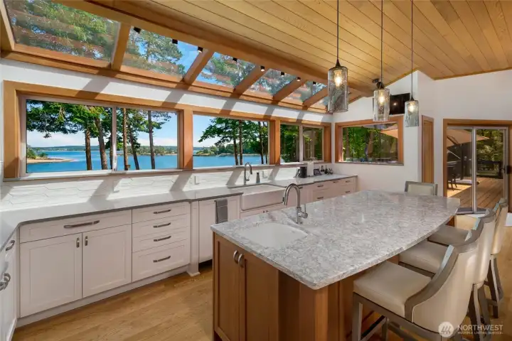 Updated kitchen with quartz countertops, generous island seating, vaulted wood ceilings, skylights, and expansive windows framing panoramic San Juan Island water views.