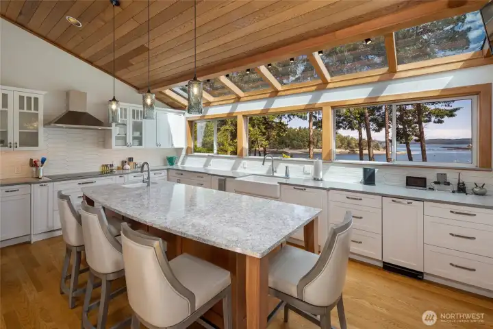 Bright open kitchen features abundant natural light, clerestory-style skylights, quartz surfaces, stainless appliances, and captivating views toward Turn Island and the surrounding waterfront.