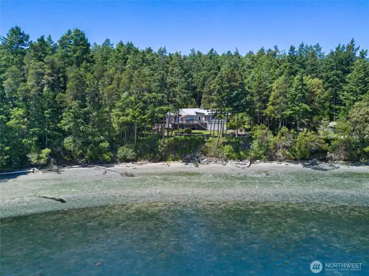 Aerial overview captures the home’s private waterfront position, beach frontage, forested acreage, and scenic location along the San Juan Island shoreline near Friday Harbor.