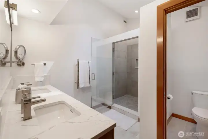 Updated guest bath features a dual-sink vanity, modern finishes, glass-enclosed tile shower, and a separate water closet for added convenience.
