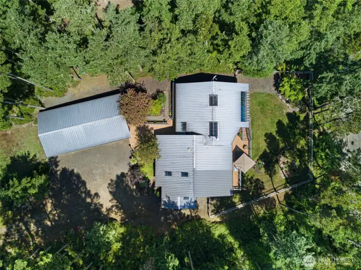 Overhead aerial view shows the home, detached garage, decks, landscaped grounds, and surrounding evergreens within the private 1+ acre waterfront setting.