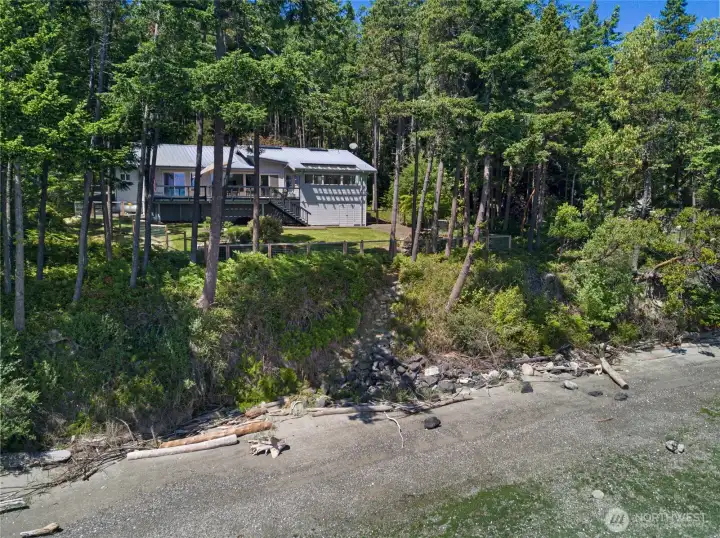 Waterfront view of the home set above the shoreline, highlighting the property’s private beach access, mature trees, and peaceful coastal setting.