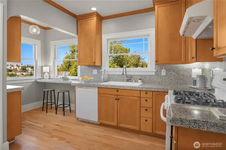 The spacious kitchen features granite counters, maple cabinetry, and a convenient breakfast bar framed by large windows with treetop and city views.