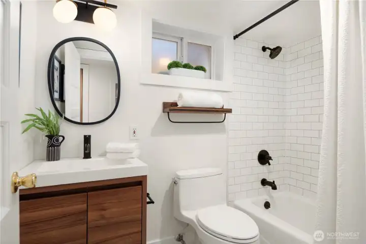The updated bath shines with modern tilework, stylish fixtures, and a shower/tub combo with matte black accents.