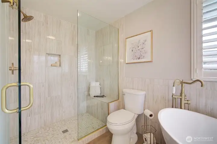 A frameless glass shower is nicely accented with a built-in bench.  Hardware is finished in rubbed gold tones.