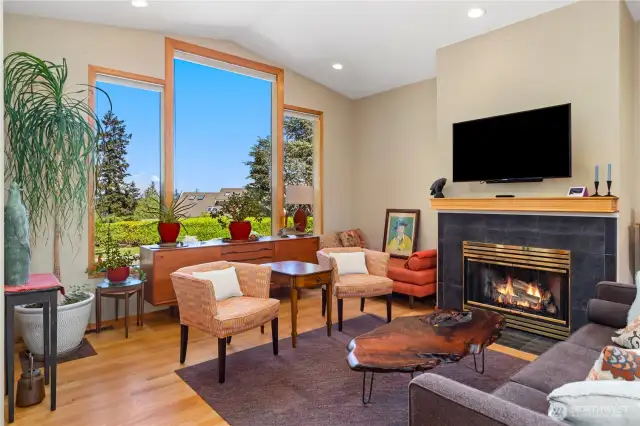 The warm and inviting living room has picture windows overlooking the patio and partial water views in the distance. A propane fireplace, hardwood floors, and beautiful wood trim windows add character and style to the room.
