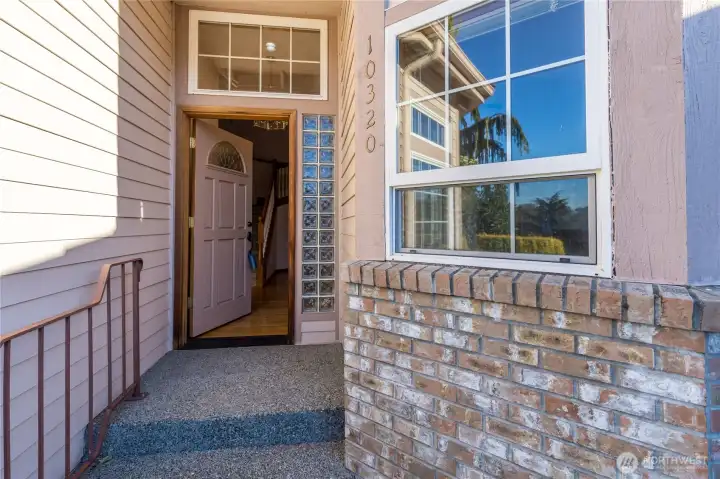 The front door is just inside a covered porch, and walkways and the driveway are textured cement aggregate.  The wrought iron railing extends to the street, and has a gate for accessing the front yard