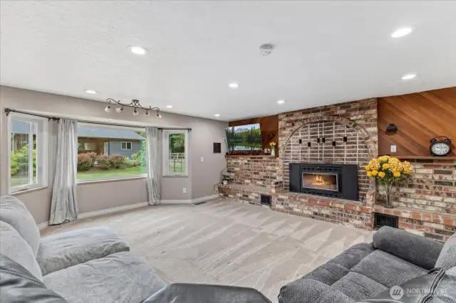 Bright and inviting Family room featuring a cozy brick fireplace, large picture windows, and ample space for relaxing or entertaining