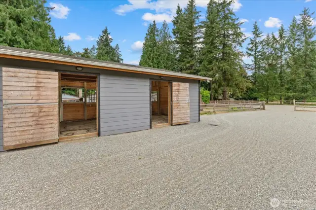 Back side of the stall barn with Dutch doors, riding paddock with mud-free hoof-grid footing under the sand and gravel.