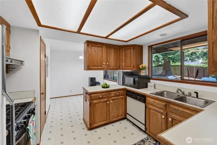 Bright and inviting kitchen featuring extensive wood cabinetry, generous workspace, and large windows that bring in natural light while offering peaceful backyard views. The practical layout flows seamlessly into the dining area, making meal prep and gathering with family and friends a breeze.