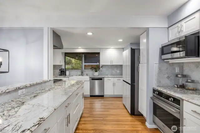 The kitchen features crisp white cabinetry, durable quartz countertops, and warm wood floors that create a timeless and inviting space.