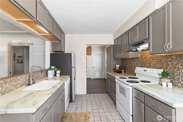 The wide and open kitchen features tile floors, modern counters and a stylish tile backsplash.