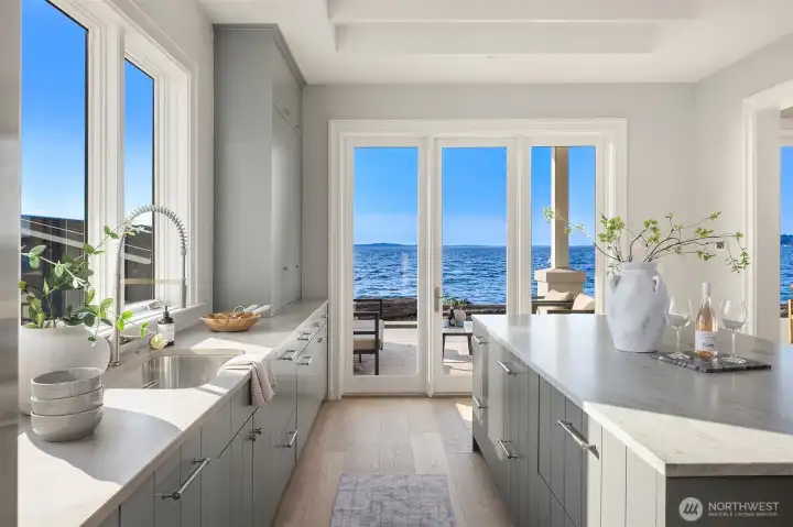 The generously sized kitchen exudes seamless coastal charm, with ample counter space and a large island that anchors the heart of the home.