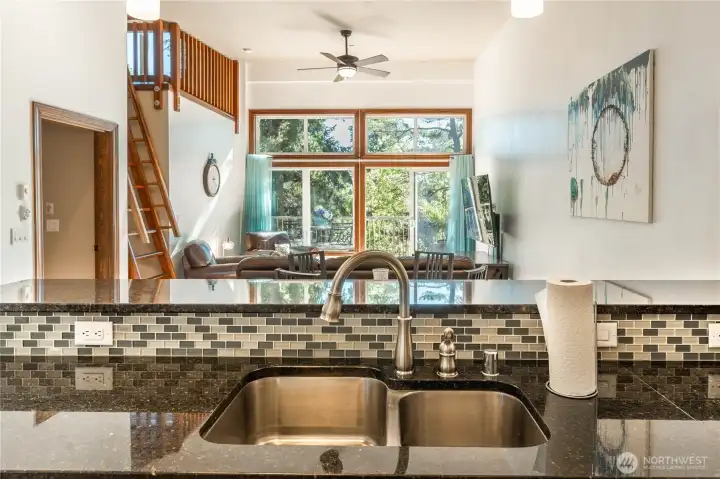 Overlooking double kitchen sink over the tiled backsplash and counter towards the living room and back deck into the trees and the southern exposure.