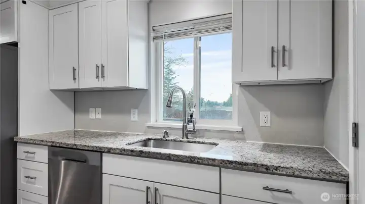 Updated kitchen with granite countertops, white cabinetry, and window over the sink for natural light.