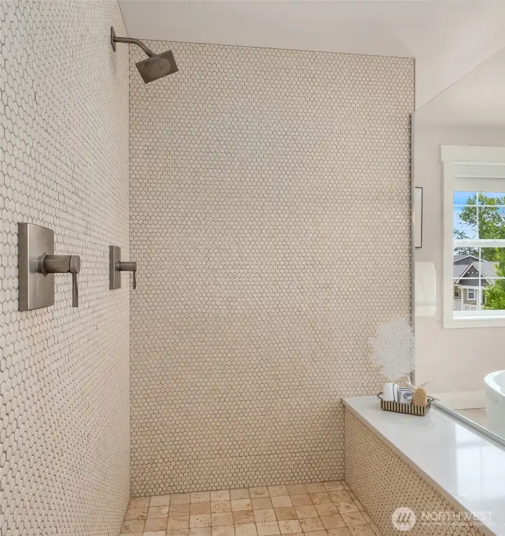 A serene spa experience awaits in the oversized walk-in shower, where floor-to-ceiling mosaic tile, heated travertine flooring, a floating quartz bench, frameless glass enclosure, and rainfall showerhead create a refined retreat. A serene spa experience awaits in the oversized walk-in shower, where floor-to-ceiling mosaic tile, heated travertine flooring, a floating quartz bench, frameless glass enclosure, and rainfall showerhead create a refined retreat.