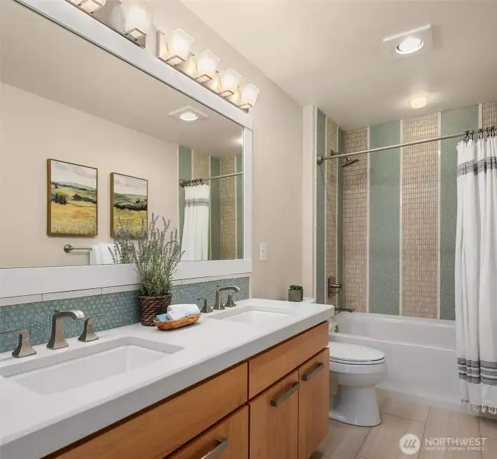 The upper-level hall bath reflects the same thoughtful craftsmanship found throughout the home, featuring a furniture-style walnut vanity with dual sinks, quartz countertops, and a striking floor-to-ceiling mosaic tile surround that adds texture, color, and timeless designer appeal. The upper-level hall bath reflects the same thoughtful craftsmanship found throughout the home, featuring a furniture-style walnut vanity with dual sinks, quartz countertops, and a striking floor-to-ceiling mosaic tile surround that adds texture, color, and timeless designer appeal.